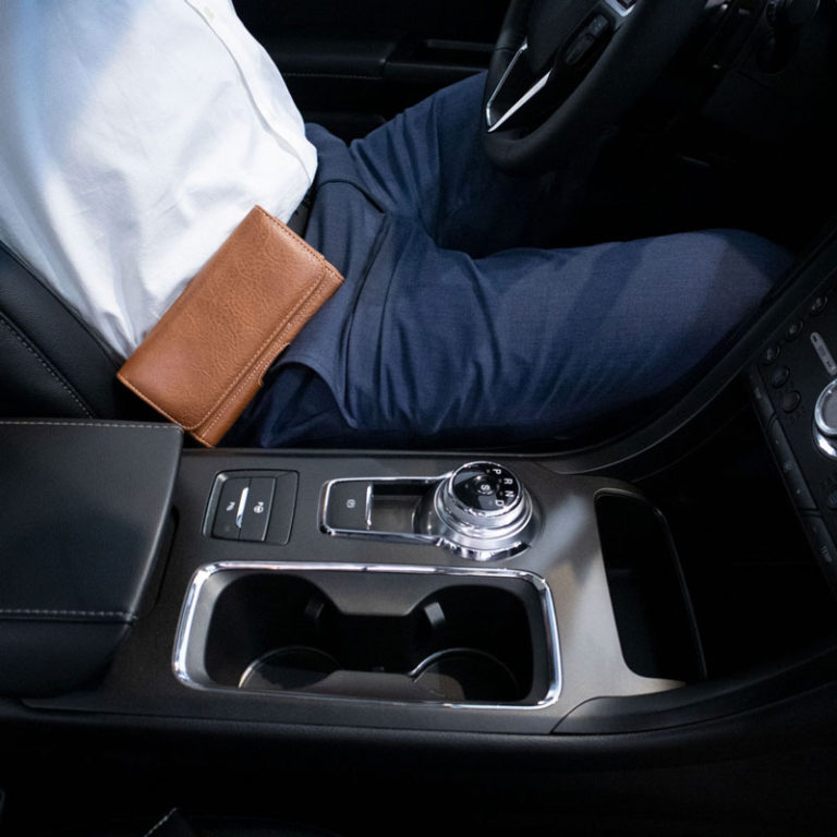 Caballero con ropa formal sentado al volante de en un coche con porta celular de cinturon cafe